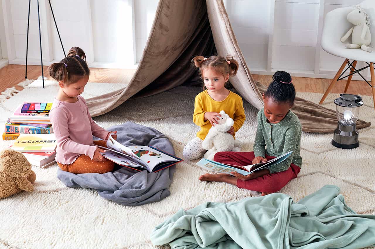 Children sitting on a bedroom floor with blankets.