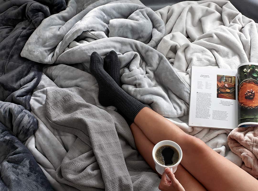 Woman laying in bed with blankets coffee and magazine.