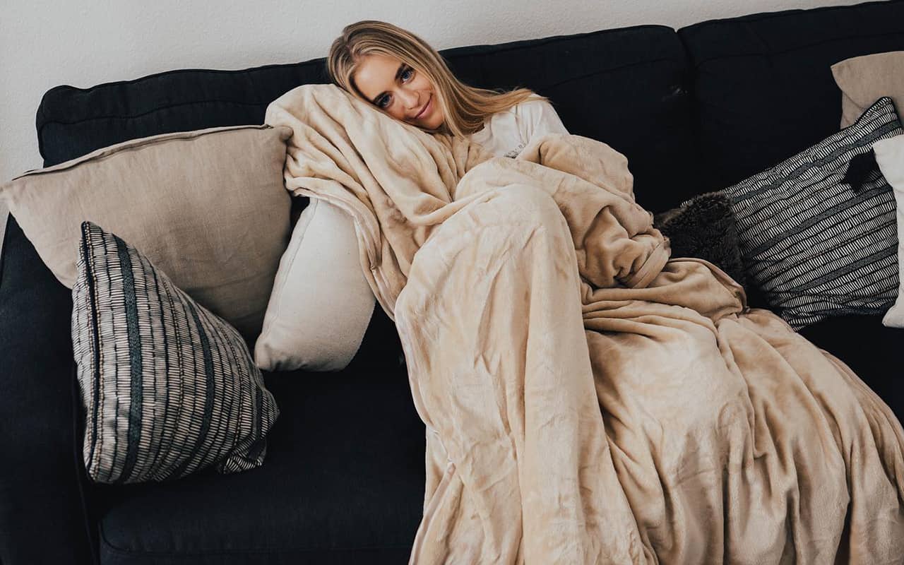 A woman covered in a blanket on a couch.